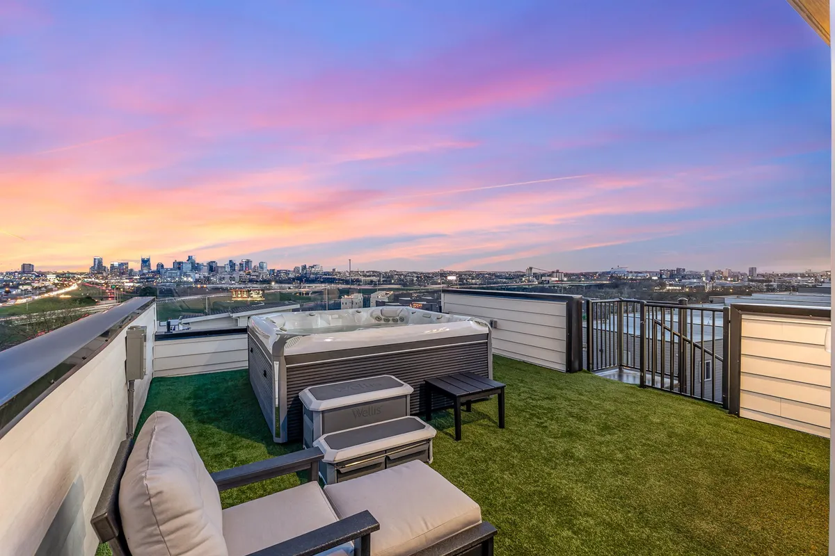 This image features a rooftop hot tub with comfortable lounge chairs, set against a striking sunset sky and panoramic city skyline. The mood is serene and inviting, perfect for showcasing relaxation and evening gatherings.