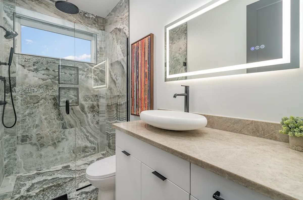 A luxurious bathroom featuring a large glass-enclosed shower, a unique stone wall for texture, a backlit mirror, and a minimalist sink. The space feels tranquil and sophisticated, ideal for relaxing self-care routines.