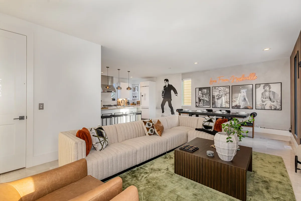 A bright and stylish interior lounge featuring a bold striped sofa, a green area rug, an Elvis mural, and a coffee table. Visible artwork and playful decor create an inviting first impression, suggesting an entry or transition area.