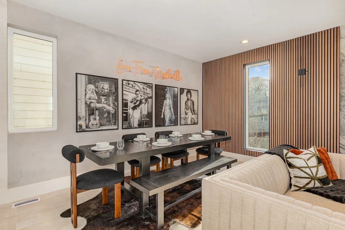 A chic dining area set for a meal, with framed photographs, a neon 'Live From Nashville' sign, and a large window providing natural light. The artistic decor and thoughtful table setting enhance the sense of occasion and warmth.