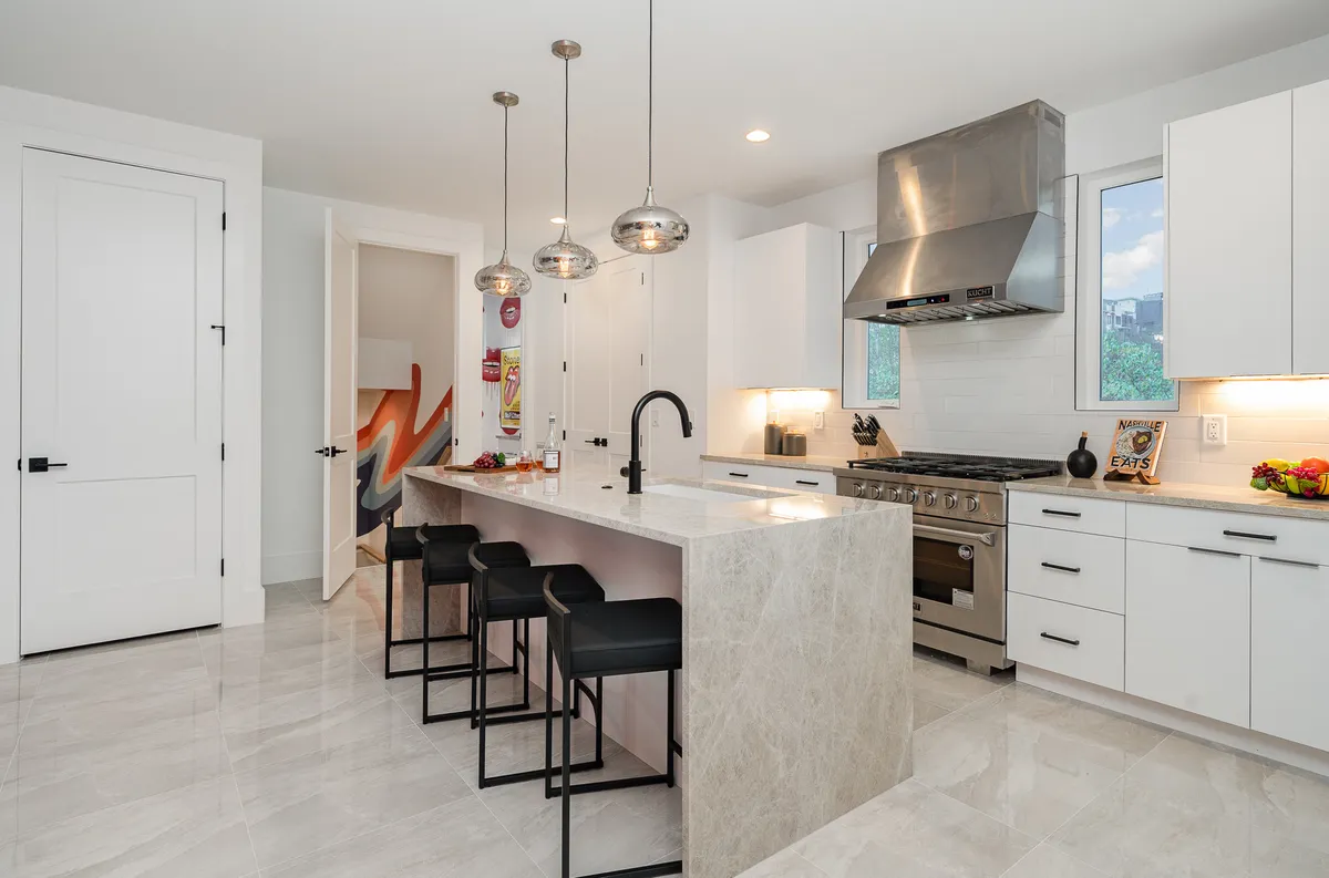 A modern kitchen with a large island, sleek stainless-steel appliances, and stylish hanging pendant lights, set within an open and welcoming layout. The space is ideal for cooking, entertaining, and casual gatherings, with plenty of room for social interaction.