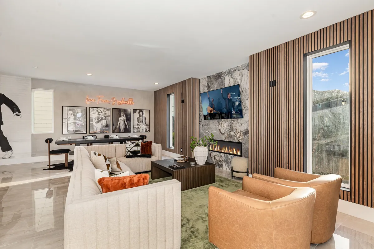A contemporary living room with a stylish sofa seating area, a cozy gas fireplace, a vibrant art wall with a neon sign, and a television screen. The room is designed for comfort and socializing, creating a welcoming atmosphere for relaxing or entertaining guests.