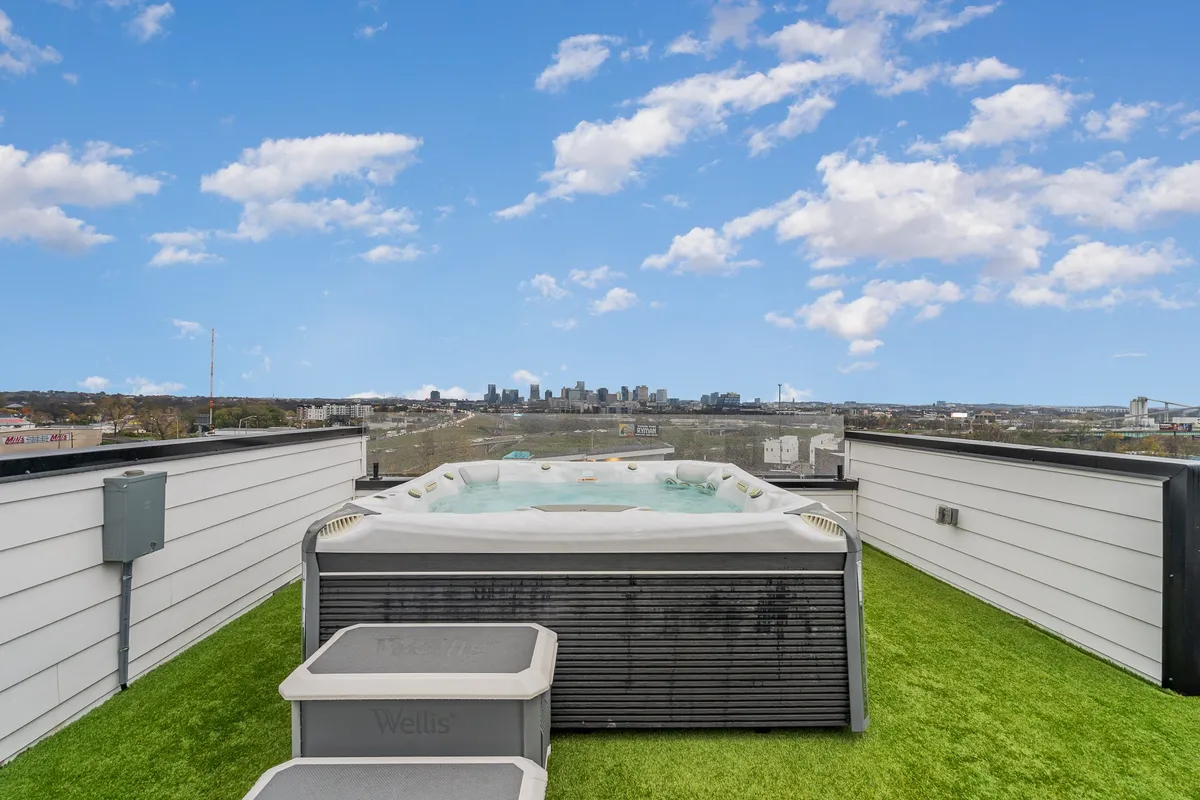 A stylish rooftop with a hot tub overlooking the Nashville skyline. The foreground features an inviting hot tub and artificial grass, while the cityscape glows in the background, suggesting luxury and relaxation above the urban excitement.